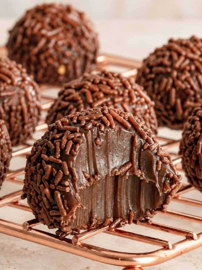 Cut-open brigadeiro revealing a fudgy chocolate center, with sprinkle-coated candies in the background.
