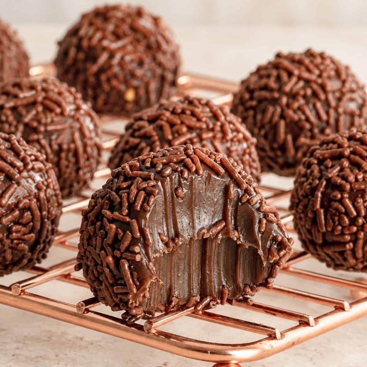 Cut-open brigadeiro revealing a fudgy chocolate center, with sprinkle-coated candies in the background.