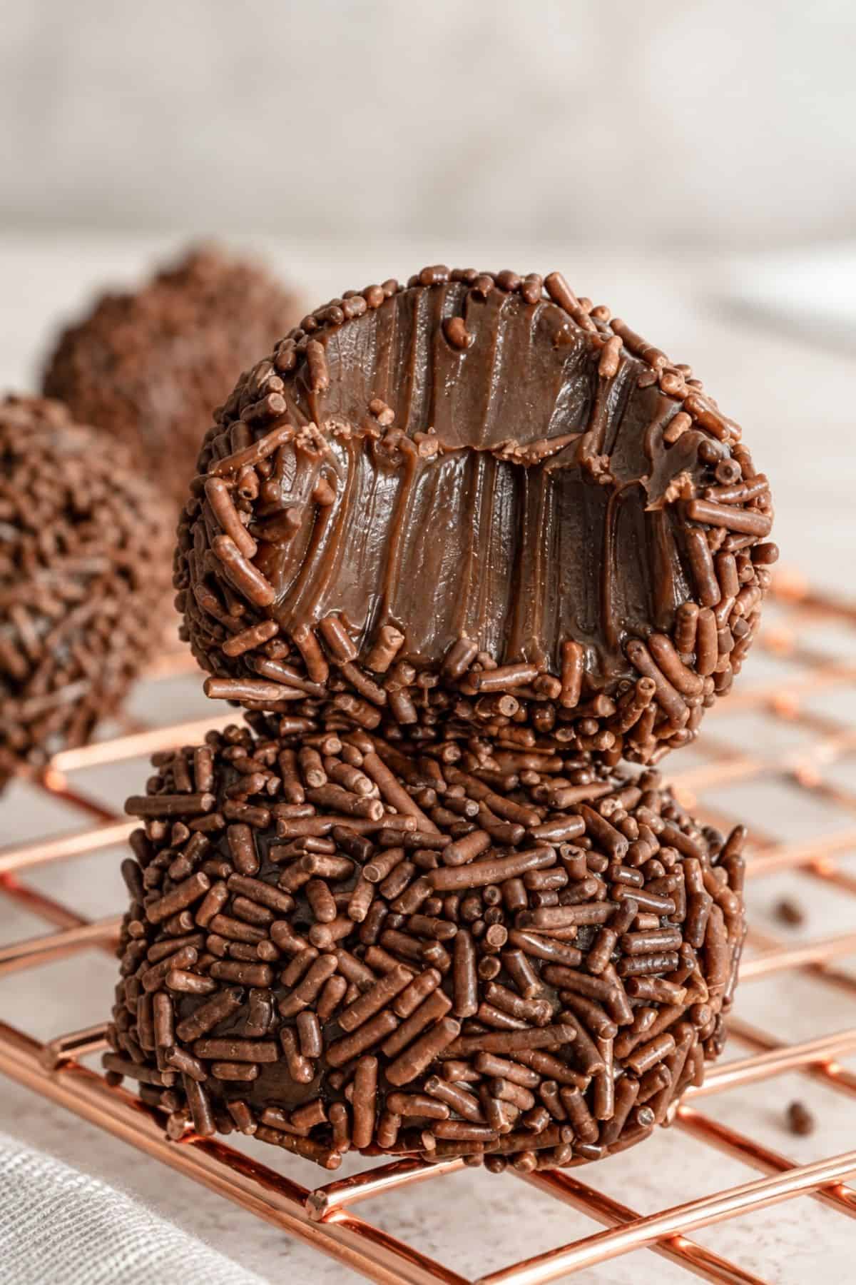 Two stacked chocolate brigadeiros, one cut open to reveal its fudgy center, on a copper wire rack.