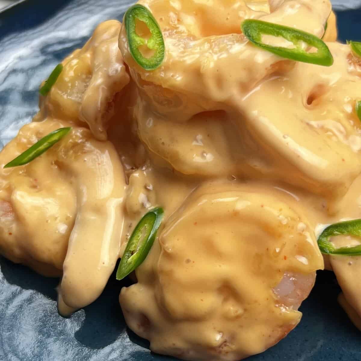 Macro shot of spicy creamy sriracha shrimp topped with fresh sliced jalapeños in a white serving bowl.