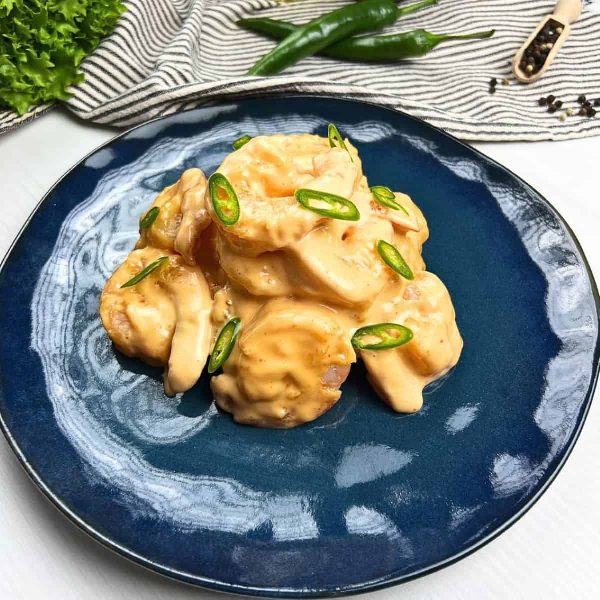 Crispy 5-Ingredient Creamy Sriracha Shrimp served on a vibrant blue ceramic plate with fresh jalapeño garnishes.