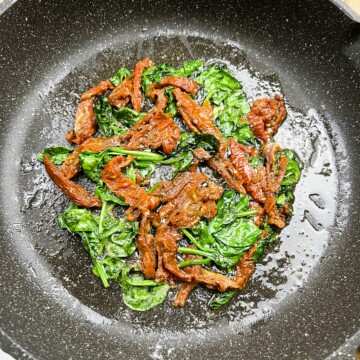 Adding the sun dried tomatoes to the skillet with spinach