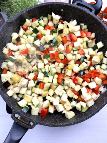diced eggplant zucchini onion and pepper cooking in skillet