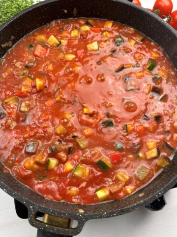 adding tomatoes and sauce to vegetable mixture in pan