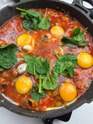 spinach added to shakshuka around eggs in skillet