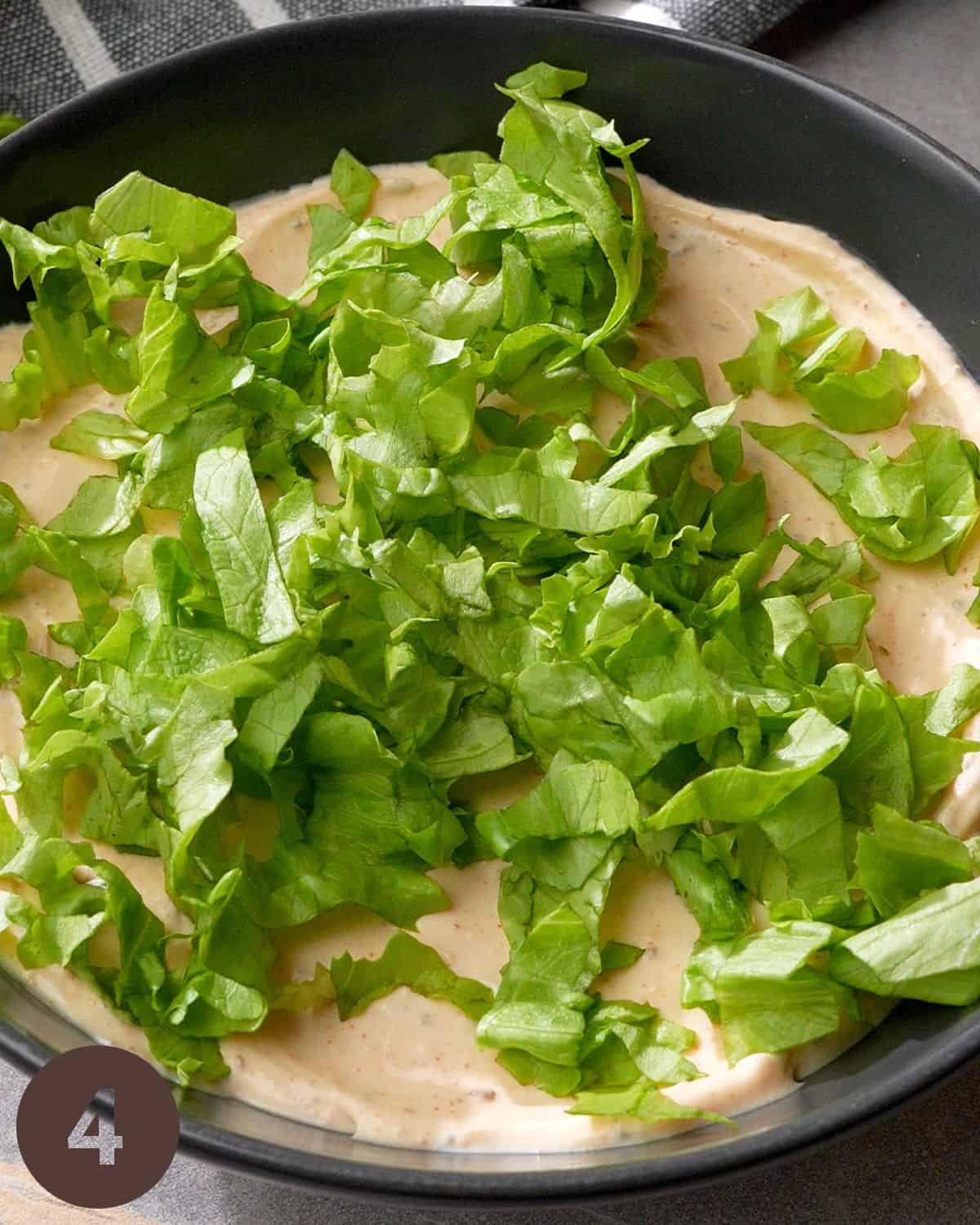 adding shredded lettuce over taco dip base layer.