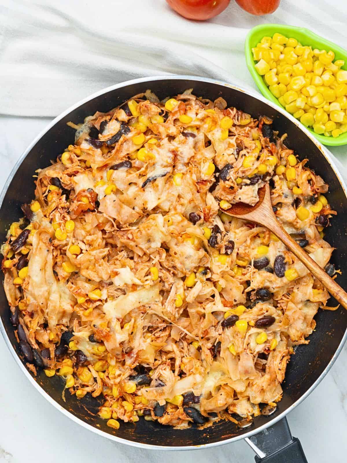 Chicken skillet enchiladas with melted cheese, tortilla strips, black beans, and corn in a skillet.
