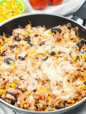 Chicken skillet enchiladas with melted cheese, tortilla strips, black beans, and corn in a skillet.