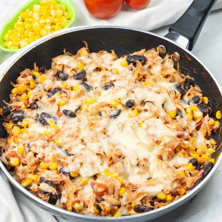 Chicken skillet enchiladas with melted cheese, tortilla strips, black beans, and corn in a skillet.