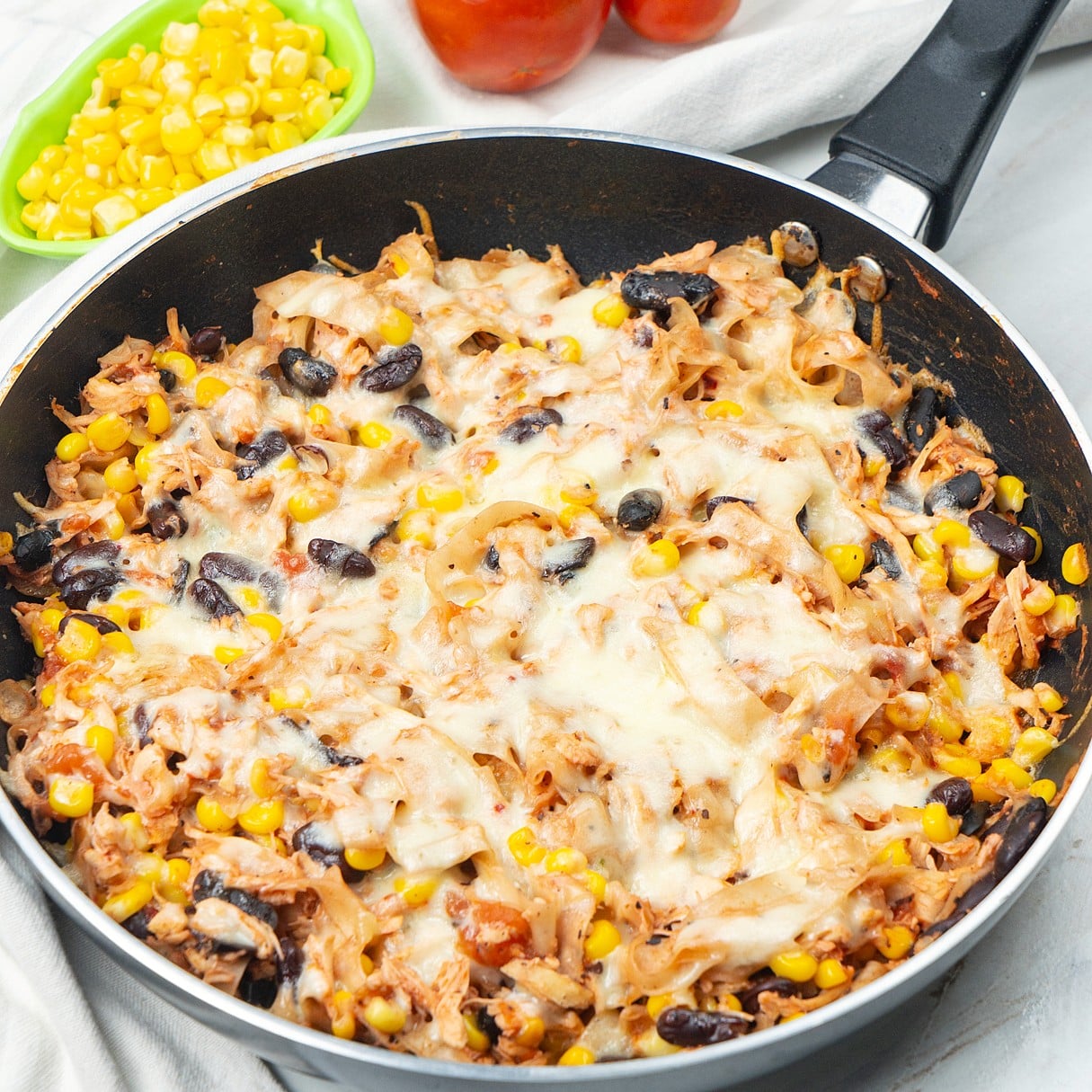 Chicken skillet enchiladas with melted cheese, tortilla strips, black beans, and corn in a skillet.