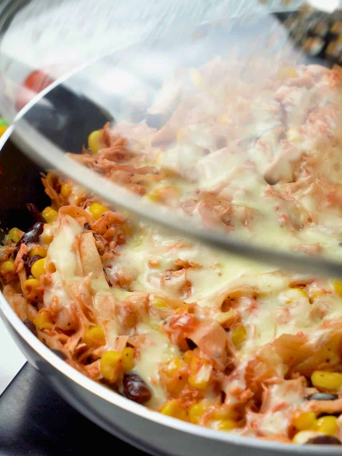 Melted cheese over chicken skillet enchiladas in skillet.