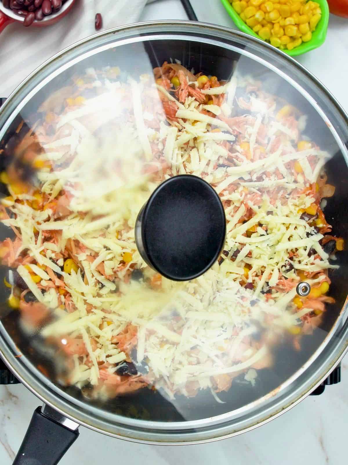 Covered skillet melting cheese for chicken skillet enchiladas.