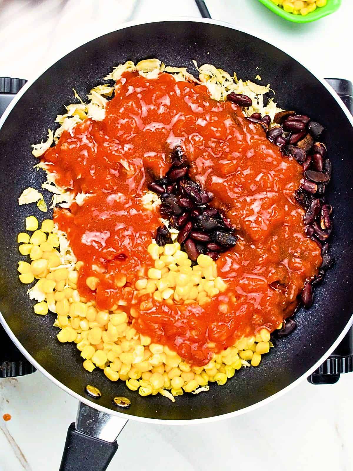 Chicken, black beans, corn, and enchilada sauce combined in skillet for chicken skillet enchiladas.