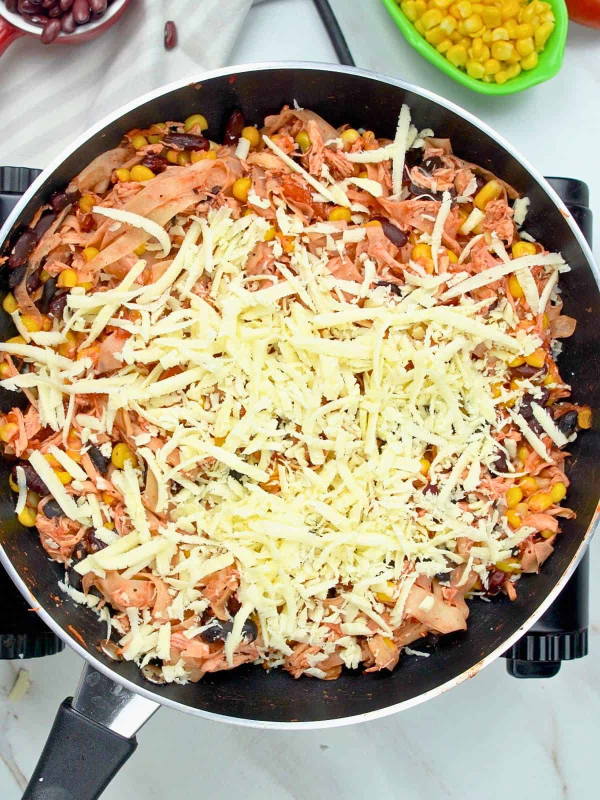 Cheese added on top of chicken skillet enchiladas.