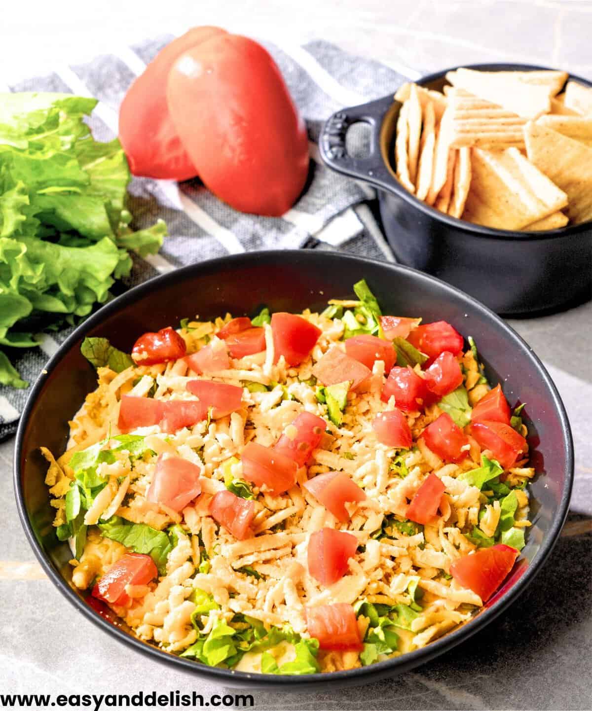 easy taco dip recipe with cream cheese lettuce and cheddar cheese in dish.
