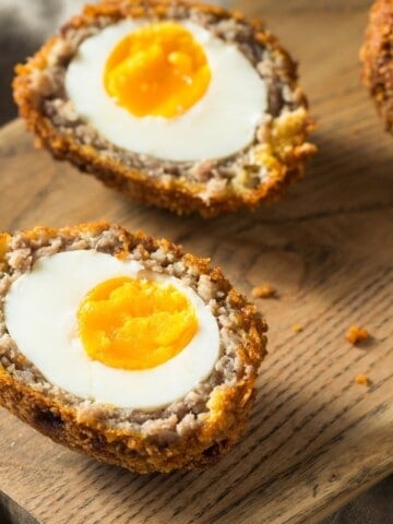 Ground beef Scotch eggs with crispy golden coating sliced in half on serving plate.