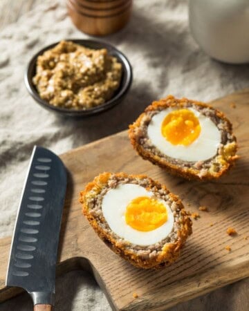 Ground beef Scotch eggs with crispy golden coating sliced in half on serving wooden board.