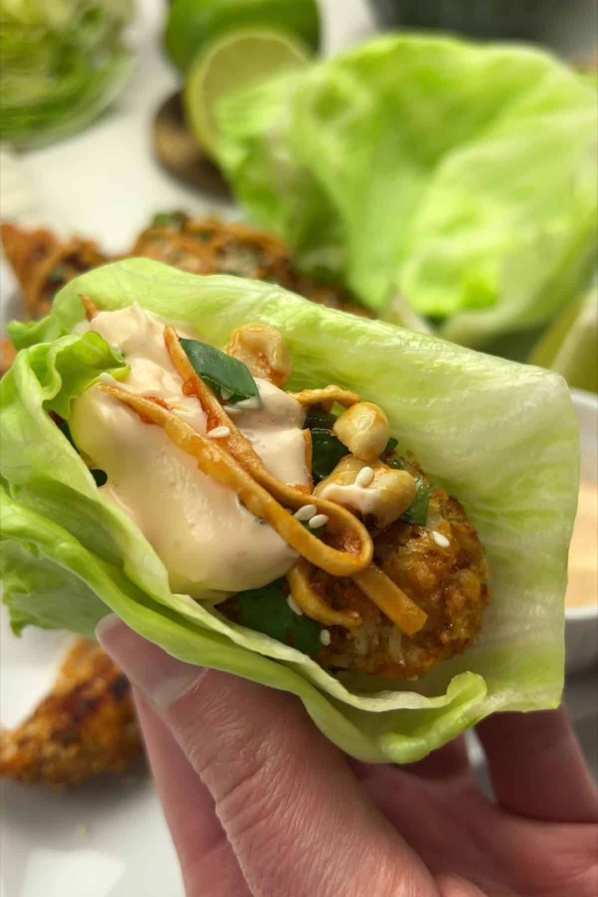 Finished close up of Szechuan chicken lettuce wraps with crispy chicken, spicy mayo, peanuts, sesame seeds, and lime.