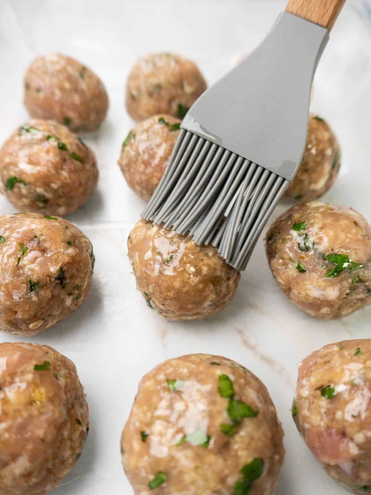Chicken Parmesan meatballs brushed with olive oil before baking.
