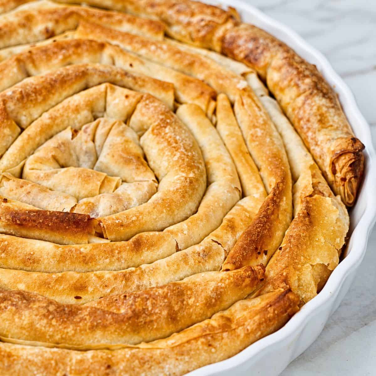 Crisp baked banitsa arranged in a spiral in a white baking dish.