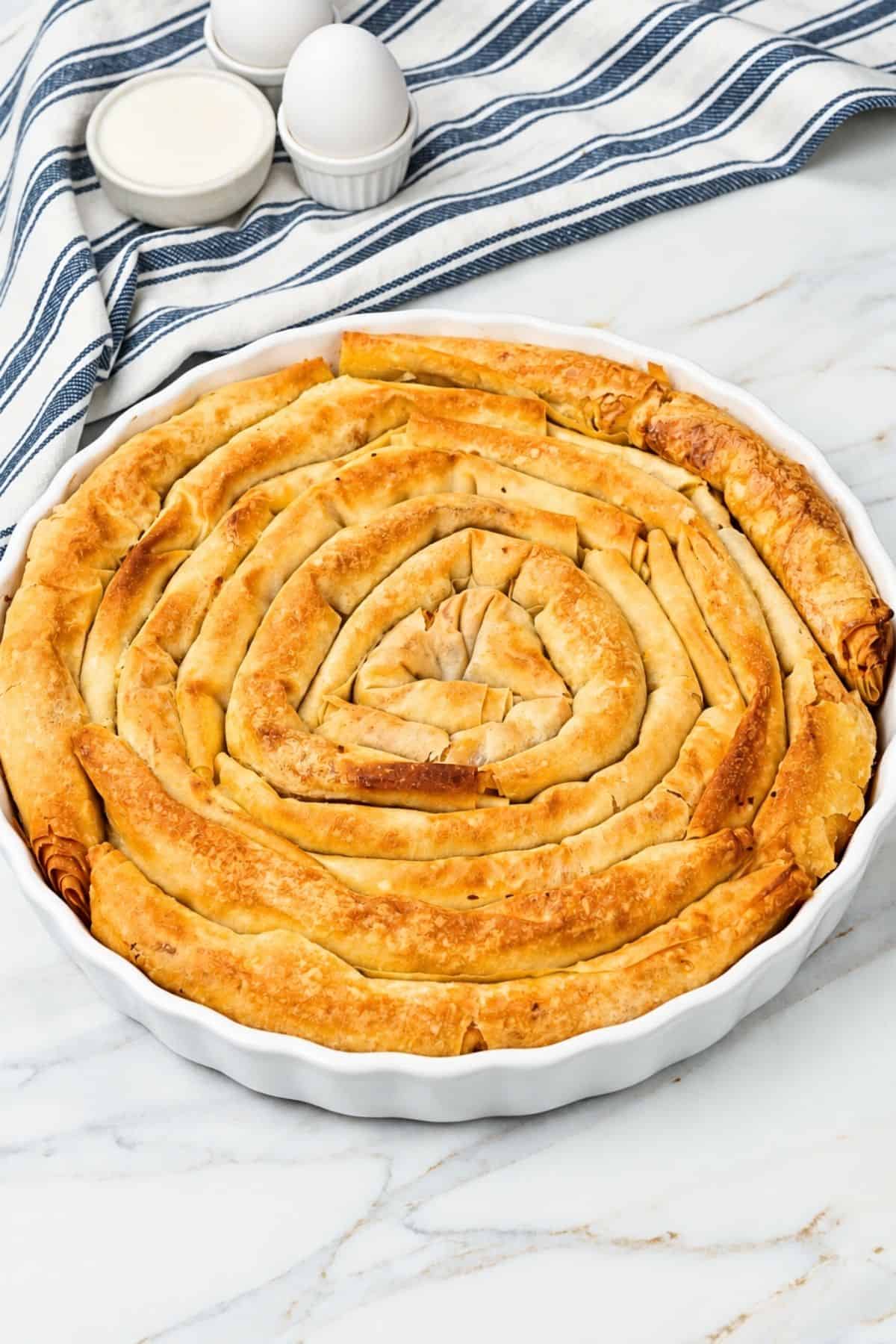 Golden spiral Bulgarian banitsa baked in a white round dish.