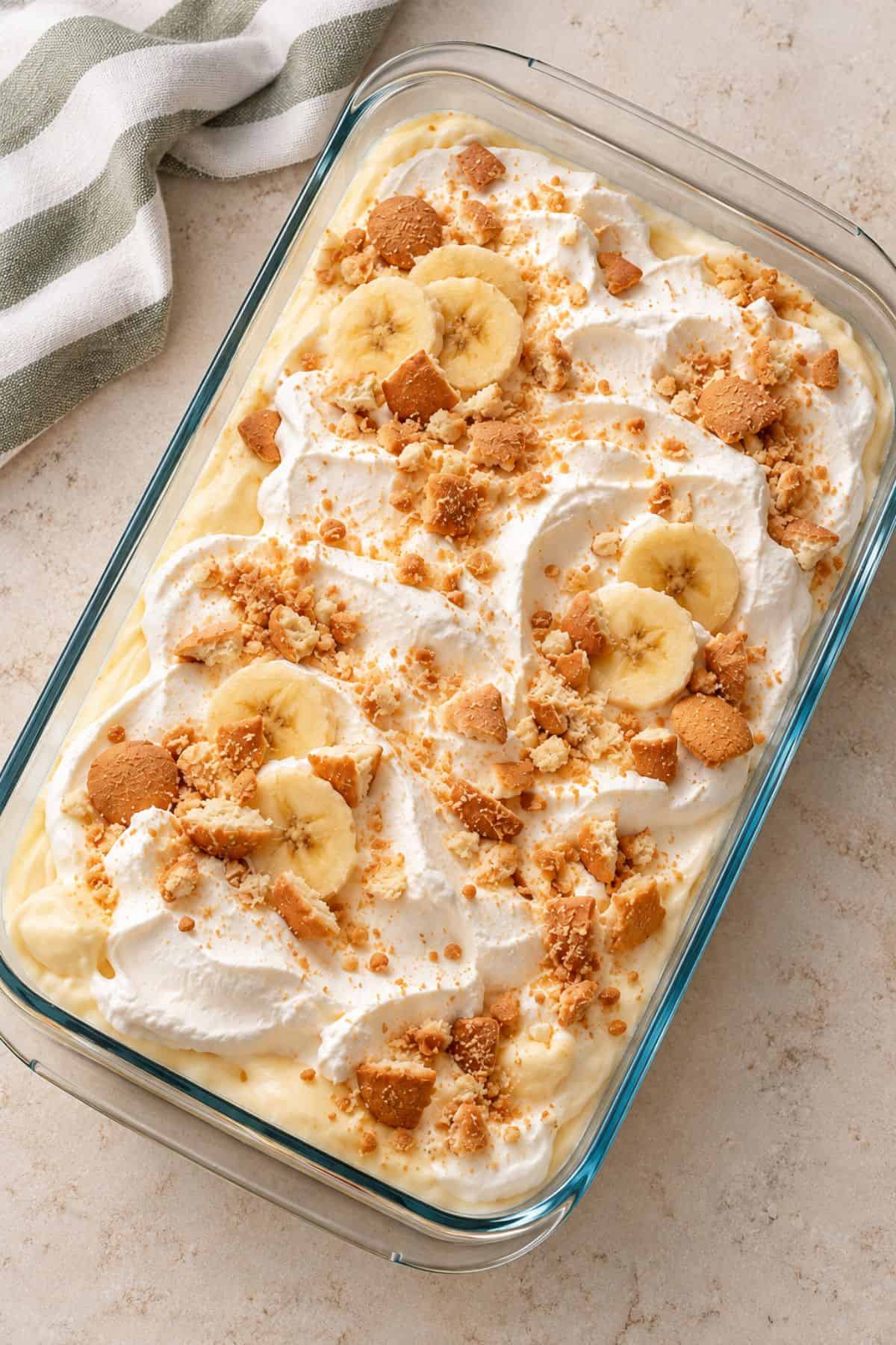 Creamy banana pudding topped with swirls of whipped cream, banana slices, and crushed cookies in a glass baking dish.