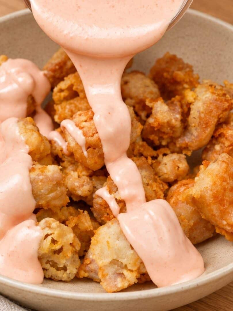 Bang Bang Sauce poured over golden, crispy chicken bites in a bowl on a table.