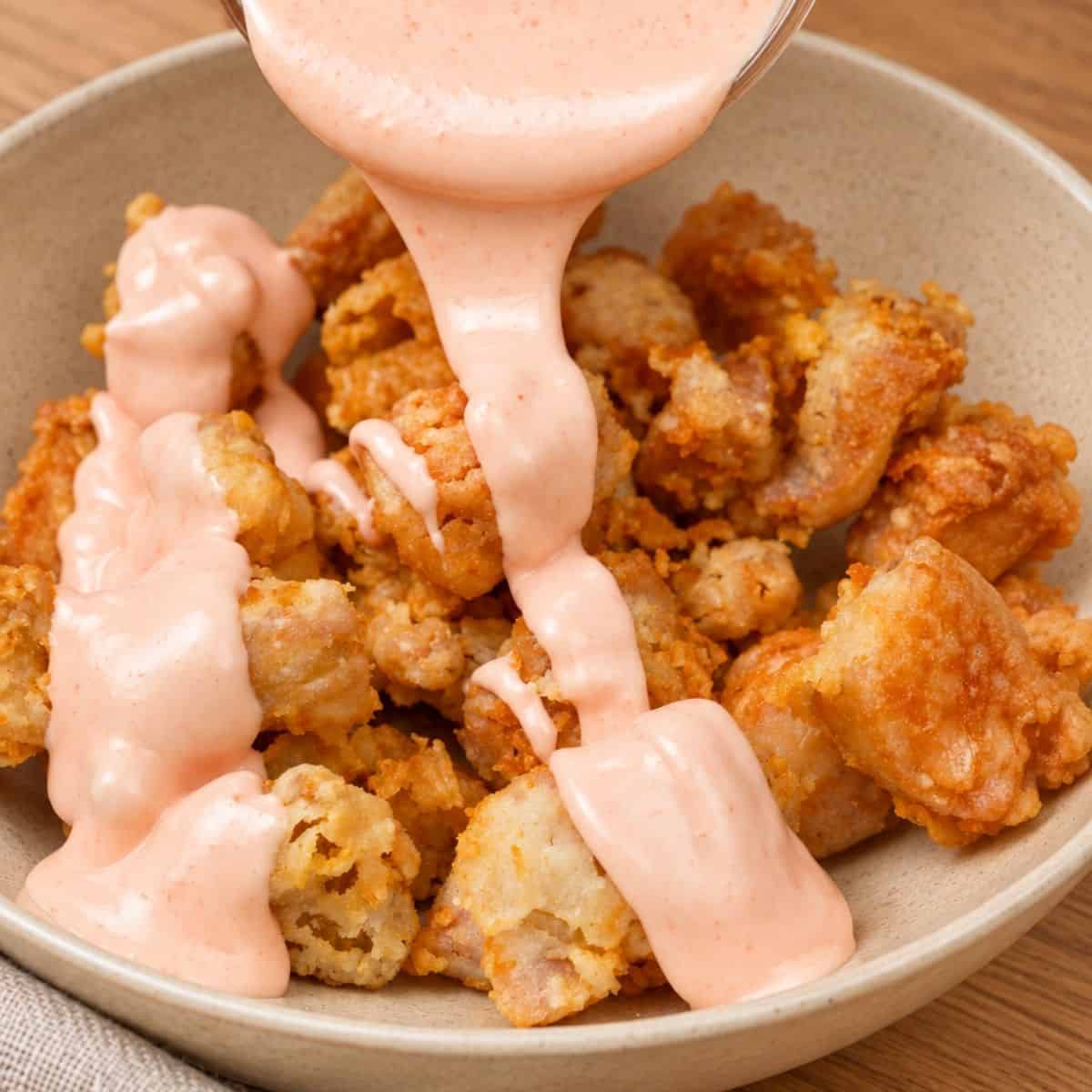 Bang Bang Sauce poured over golden, crispy chicken bites in a bowl on a table.