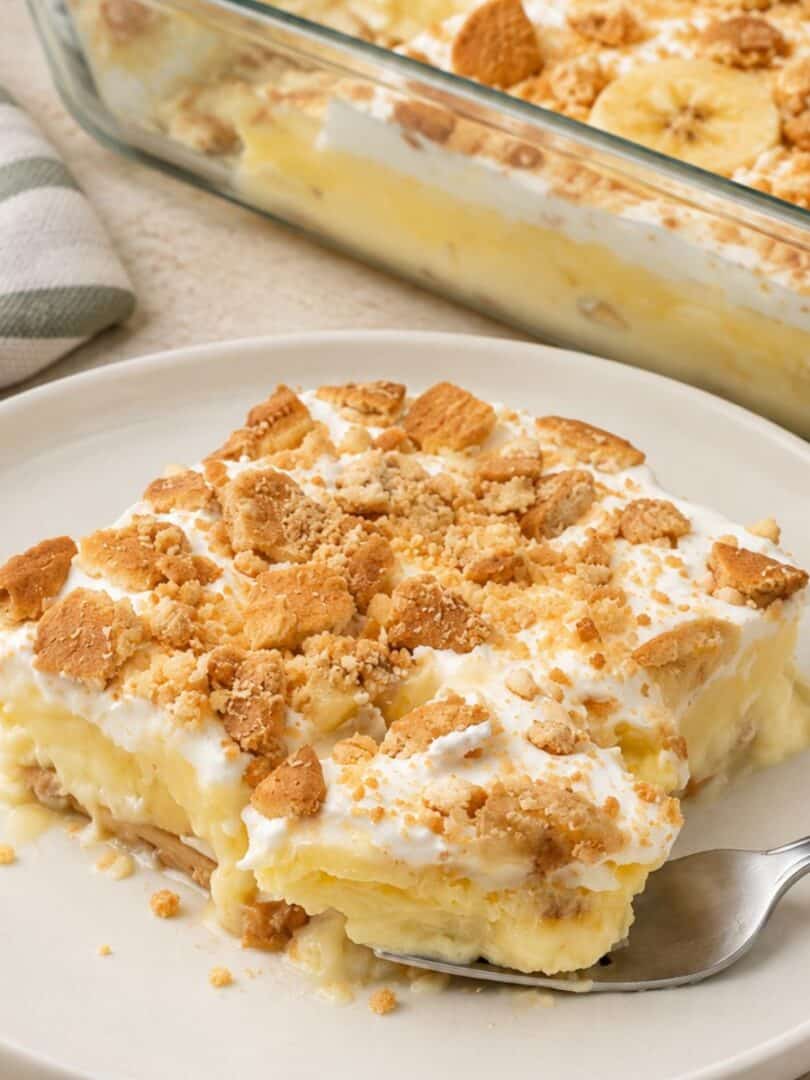 A fork holds a portion of creamy banana pudding topped with crushed vanilla wafers over a white plate.