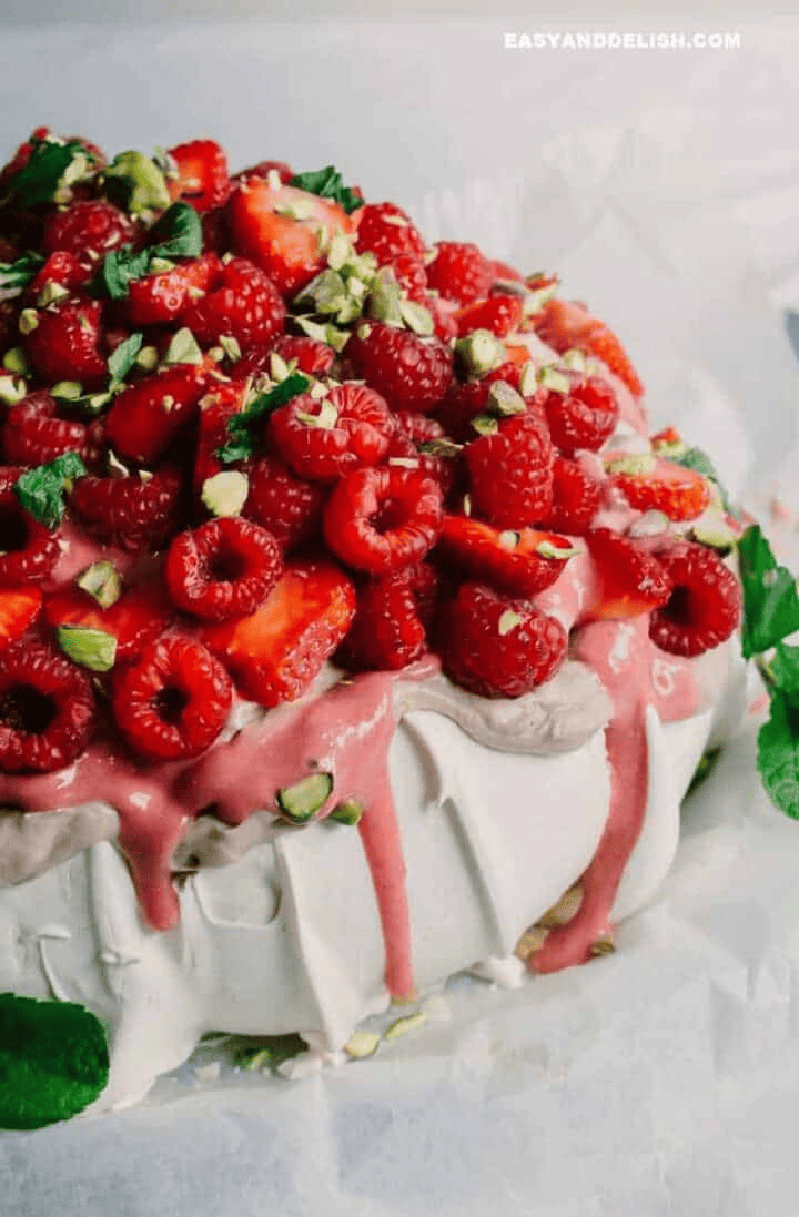 Christmas pavlova with chocolate cream, raspberry curd, fresh strawberries and raspberries, chopped pistachios, and mint on a crisp meringue base.